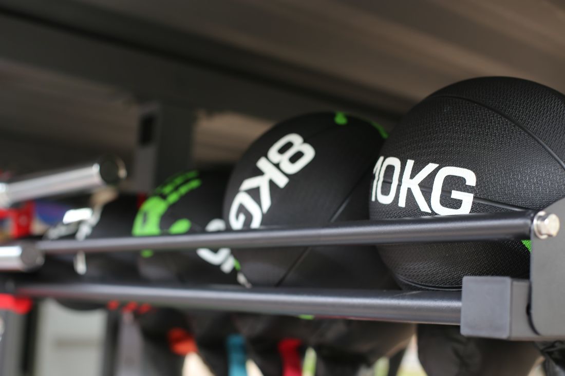 Outdoor Fitness: Medicine balls, 8kg and 10kg, on a rack. Black balls with white weight markings. Fitness equipment for outdoor workouts.